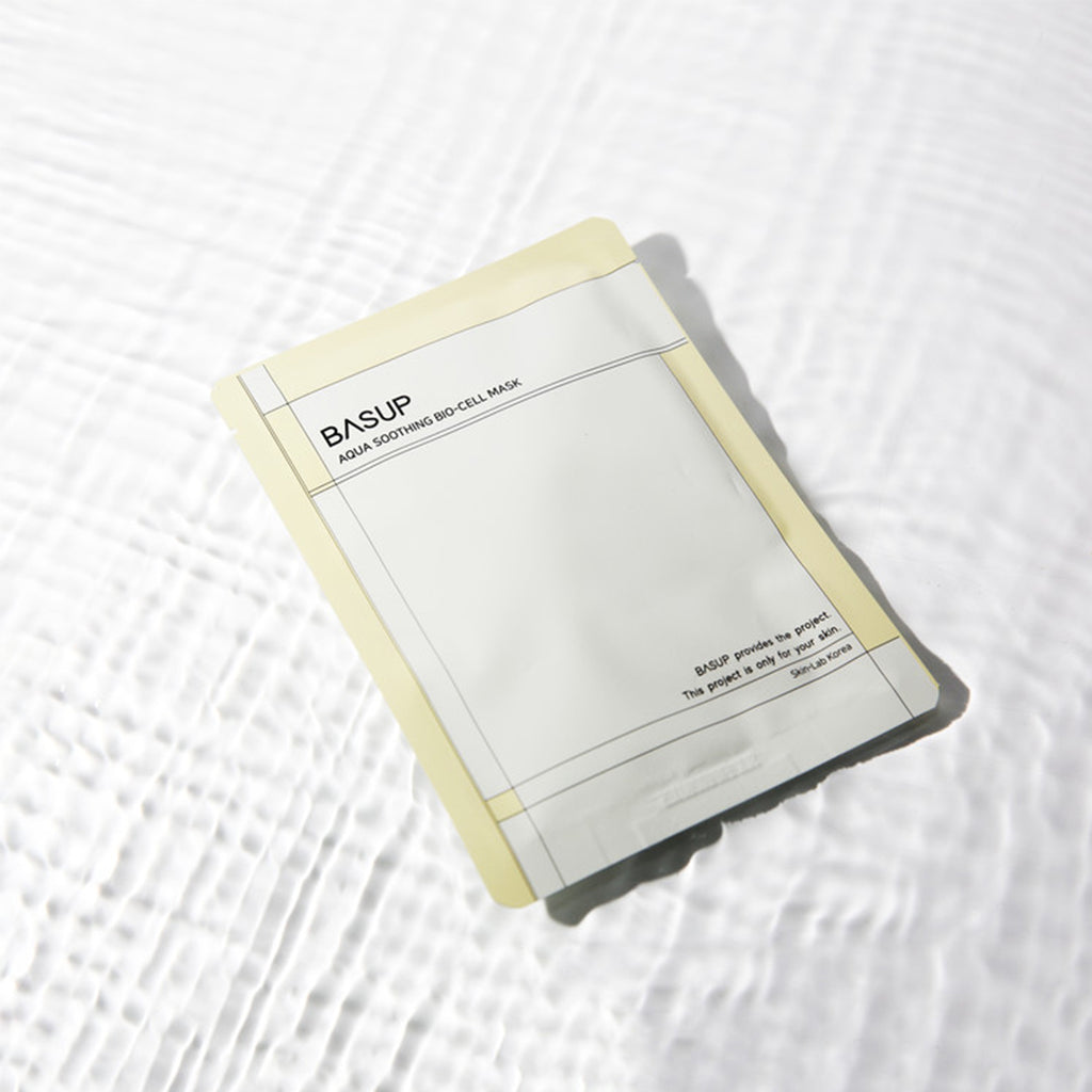 BASUP Aqua Soothing Bio Cell Mask packet with pale yellow edges on a white background with rippling water reflections.