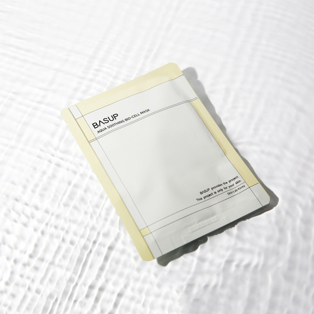 BASUP Aqua Soothing Bio Cell Mask packet with pale yellow edges on a white background with rippling water reflections.