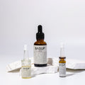 BASUP essence in an amber dropper bottle with two small ampoules displayed on white stone slabs.